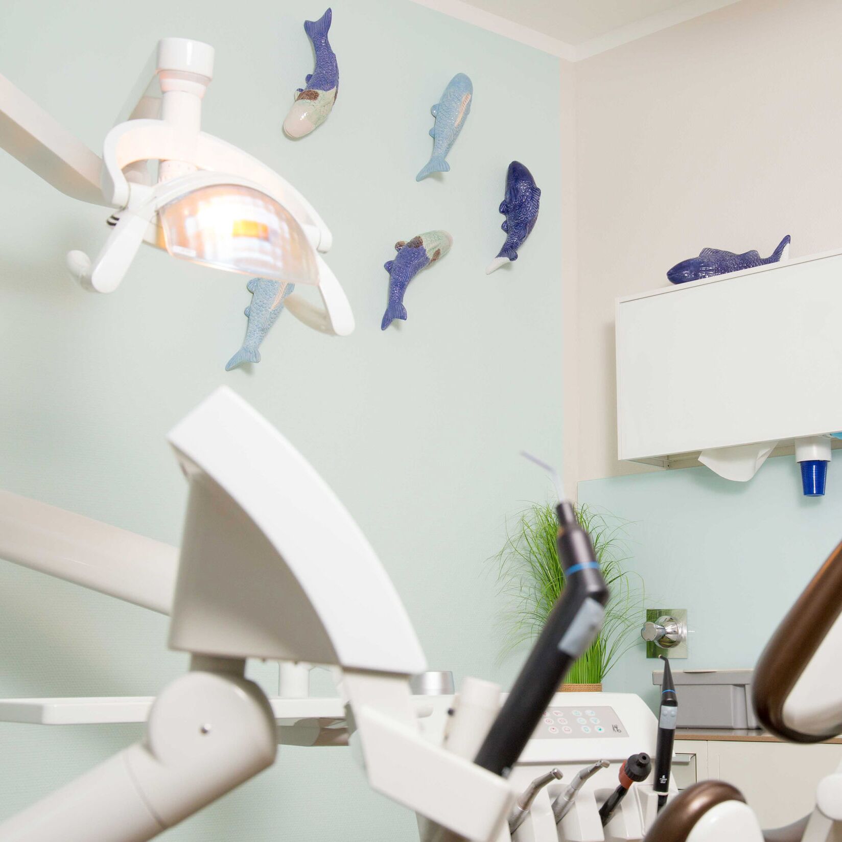 Freundlich eingerichtetes Zahnarzt-Behandlungszimmer mit Behandlungsstuhl, Zahnarztmöbeln und dekorativen Fisch-Ornamenten an der Wand