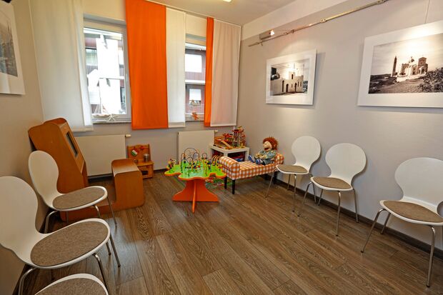 Wartezimmer der Praxis mit großem Kinderbereich und vielen Stühlen ringsrum angeordnet