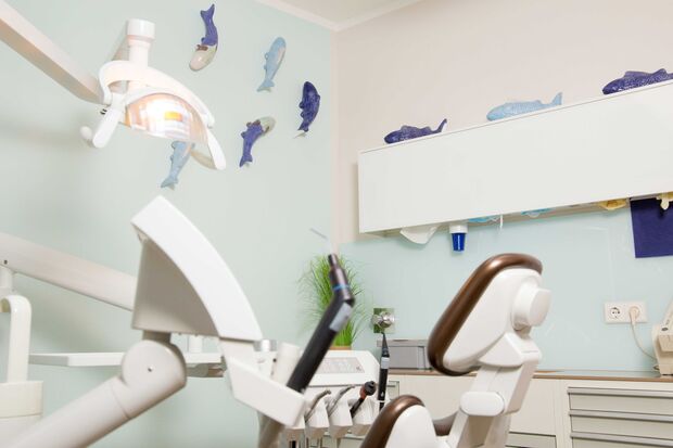 Freundlich eingerichtetes Zahnarzt-Behandlungszimmer mit Behandlungsstuhl, Zahnarztmöbeln und dekorativen Fisch-Ornamenten an der Wand